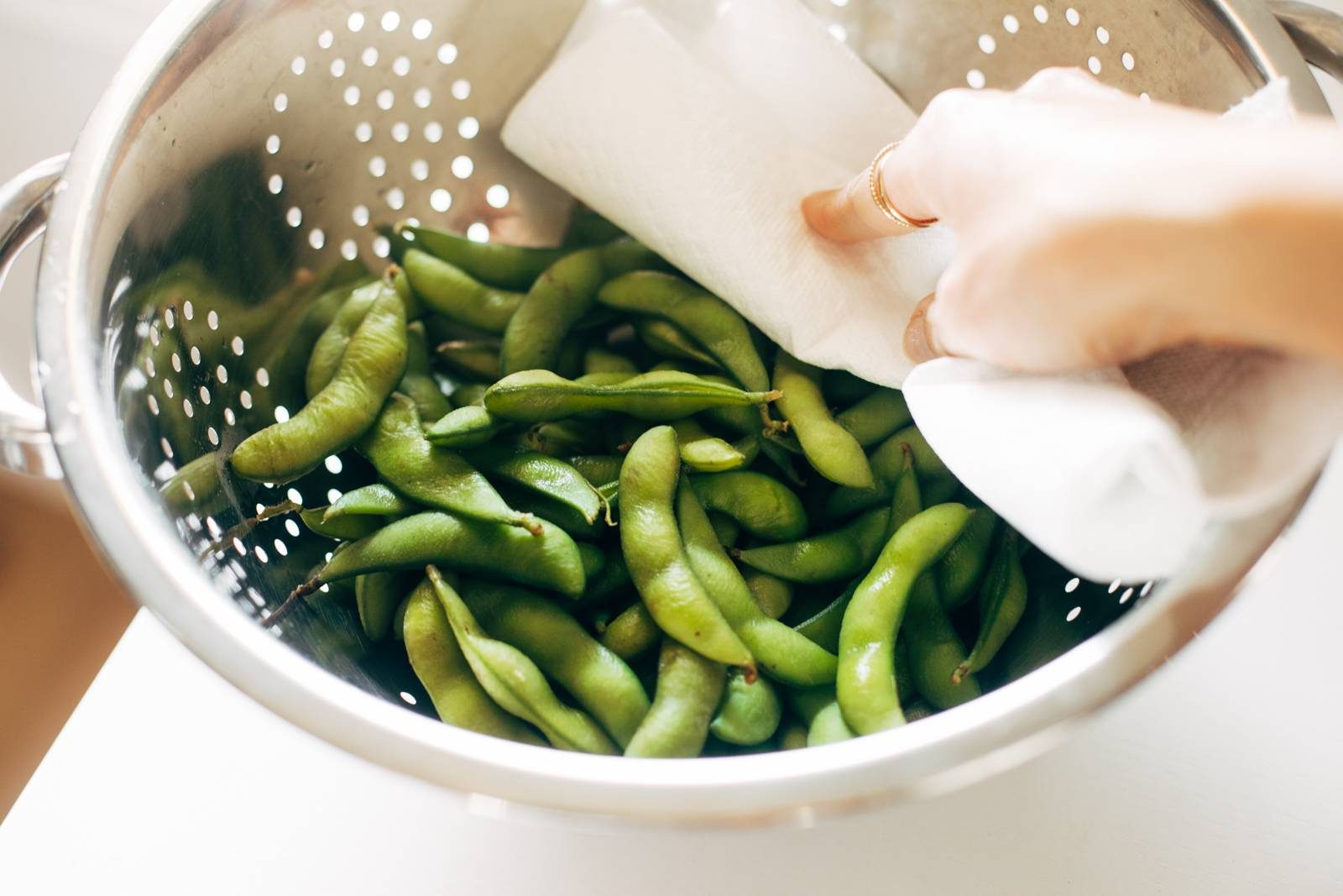 Patting boiled edamame dry with a paper towel.