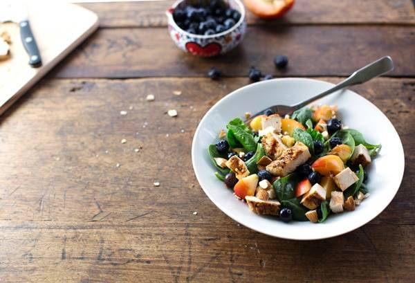 Chicken and nectarine poppy seed salad in a white bowl on a wooden surface.